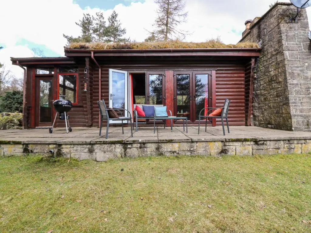 a cabin with a deck with chairs and a grill at Rocksite in Blairgowrie