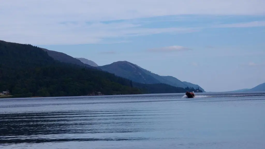 a boat on the water with mountains in the background at Abbey Garden at the Highland Club in Fort Augustus