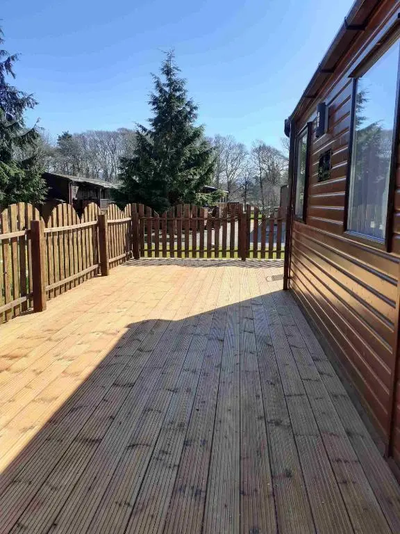 a wooden deck next to a house with a fence at Cabin 38 in Aviemore