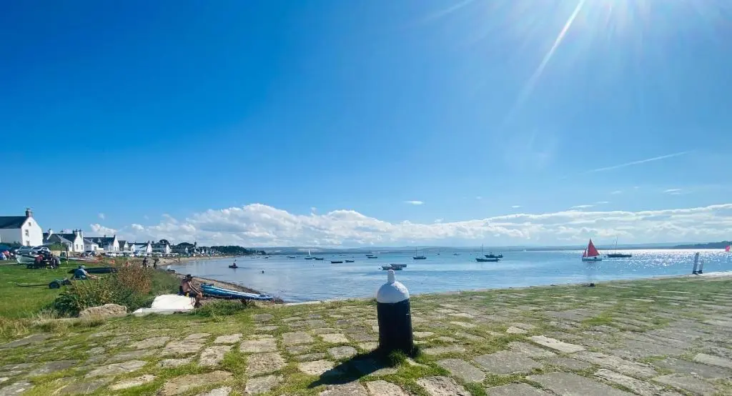 a bottle on the shore of a beach with boats in the water at Nana Cottage , Findhorn Village in Findhorn