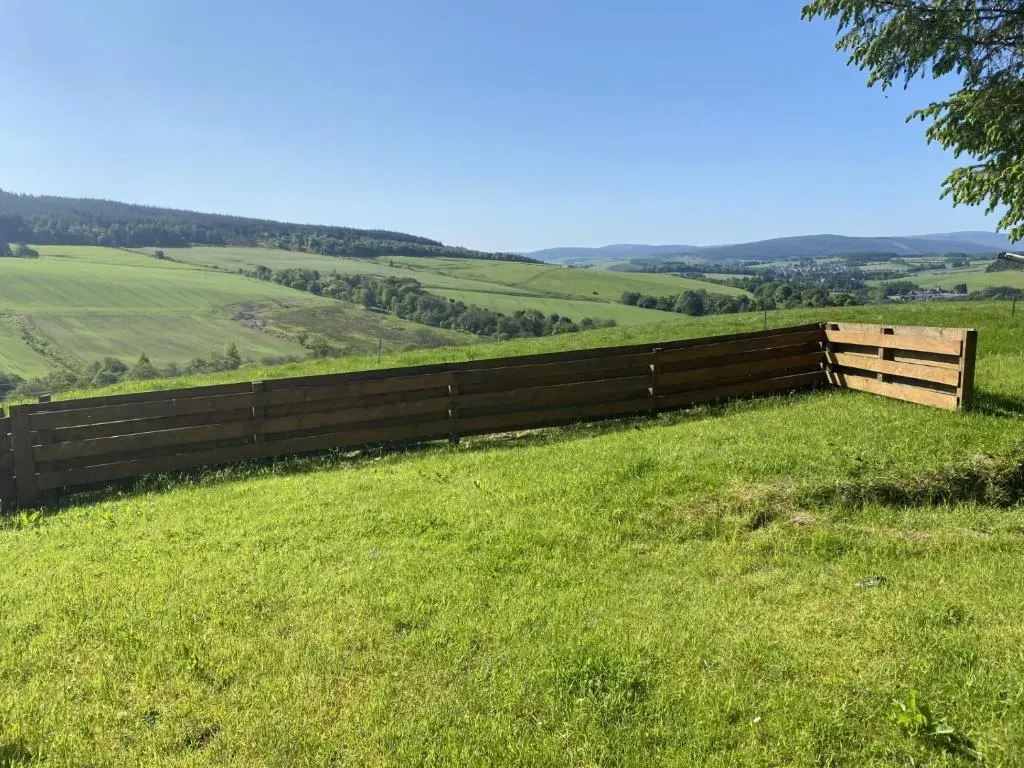 a fence on a hill with a green field at Broomhead Cottages in Dufftown