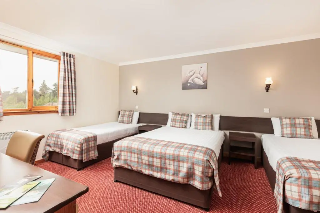 a hotel room with two beds and a table at Highlander Hotel \u2018A Bespoke Hotel\u2019 in Newtonmore