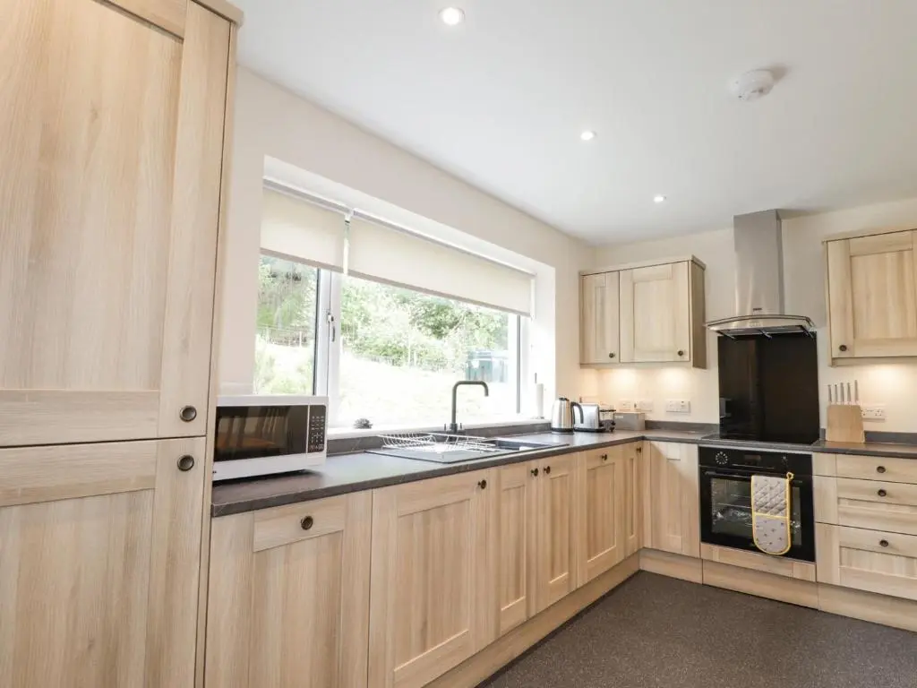 a kitchen with wooden cabinets and a window at Crask Bungalow in Beauly