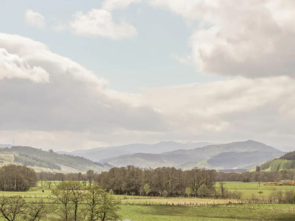 a field with trees and mountains in the background at Crask Bungalow in Beauly