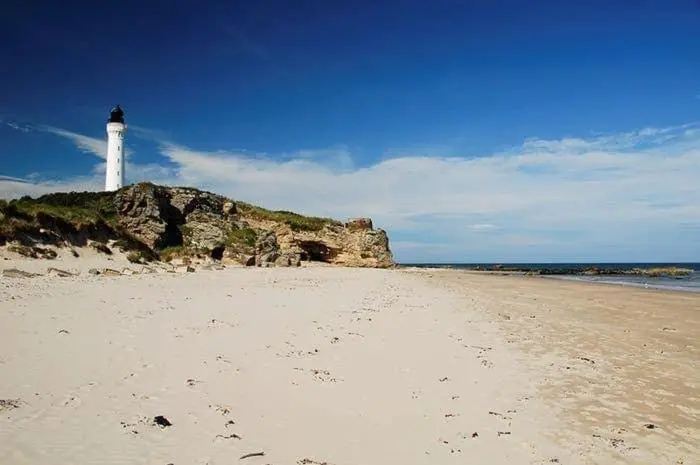a lighthouse on a sandy beach with a lighthouse at Highway in Lossiemouth