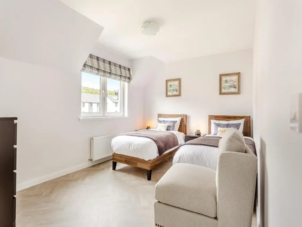 a bedroom with two beds and a chair at The Beech House in Aviemore