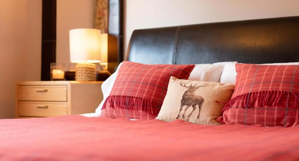 a bed with red pillows with a deer on it at Four Pines Lodge in Skye of Curr