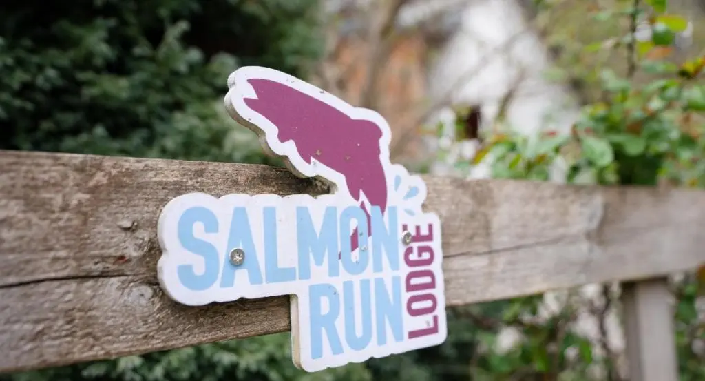 a sign on a wooden fence with a pink dog on it at Salmon Run Lodge in Carrbridge