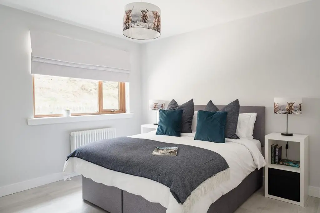 a bedroom with a large bed with blue pillows at Gardeners Cottage - Seasgair Lodges in Aviemore