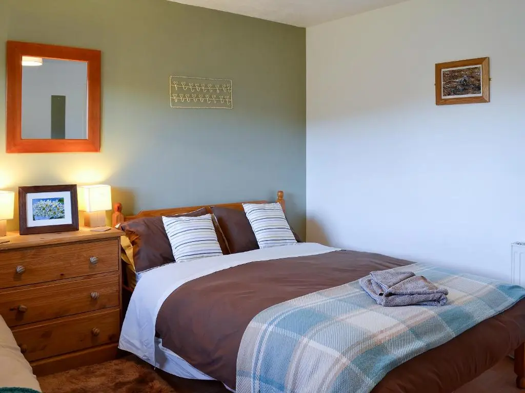 a bedroom with a bed and a dresser with a mirror at Honey Cottage in Auchnarrow