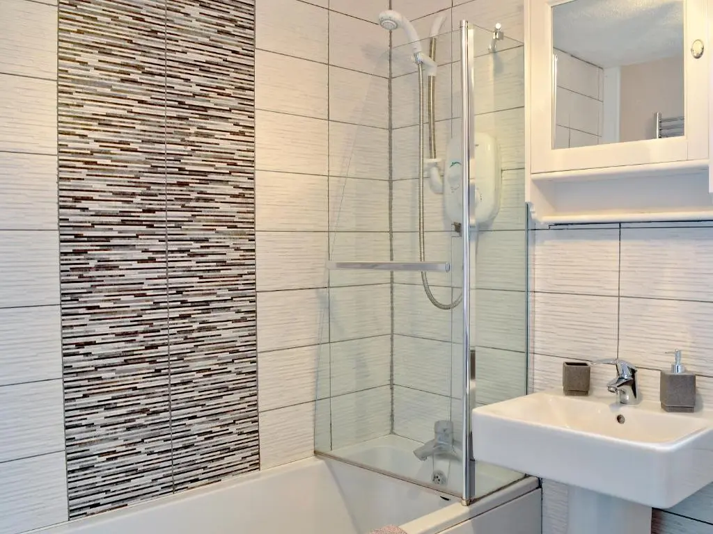 a bathroom with a glass shower and a sink at Honey Cottage in Auchnarrow