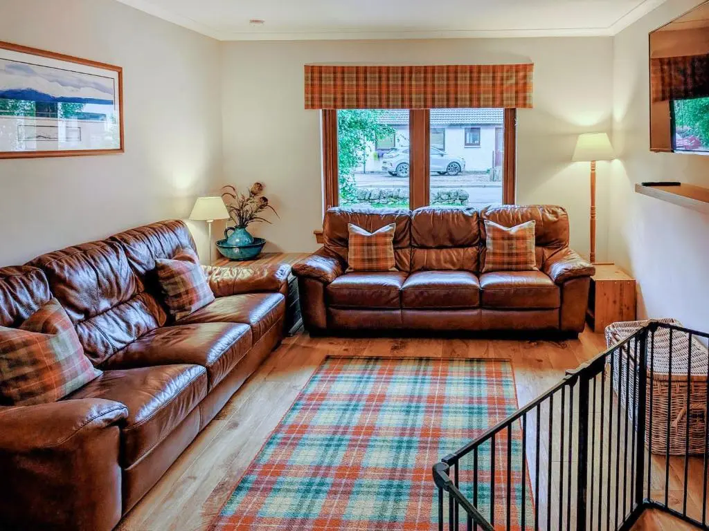 a living room with a leather couch and a rug at Rowan Cottage in Carrbridge