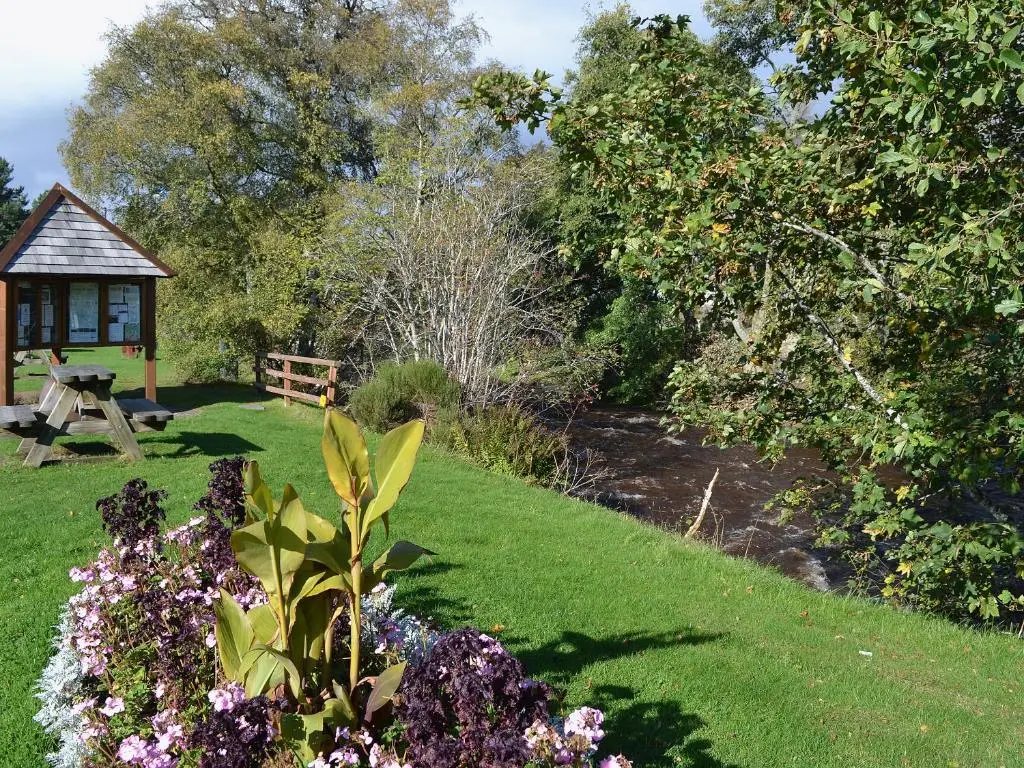 a garden with a bench and a table and flowers at Clunymhore in Nethy Bridge