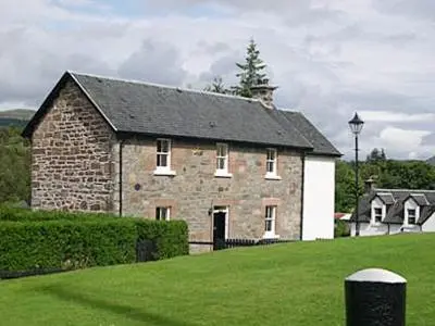 an old brick building with a black roof on a green field at Lockside Lower Flat in Fort Augustus