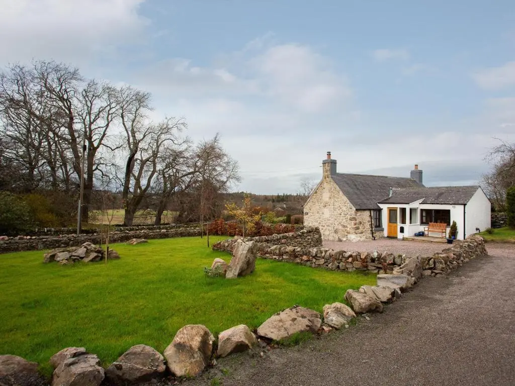 a stone house with a yard and a stone wall at Craigellachie Cottage in Croy