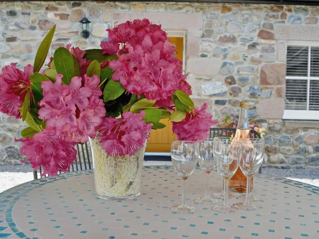 a vase with pink flowers on a table with wine glasses at Ladybird Cottage in Lochend