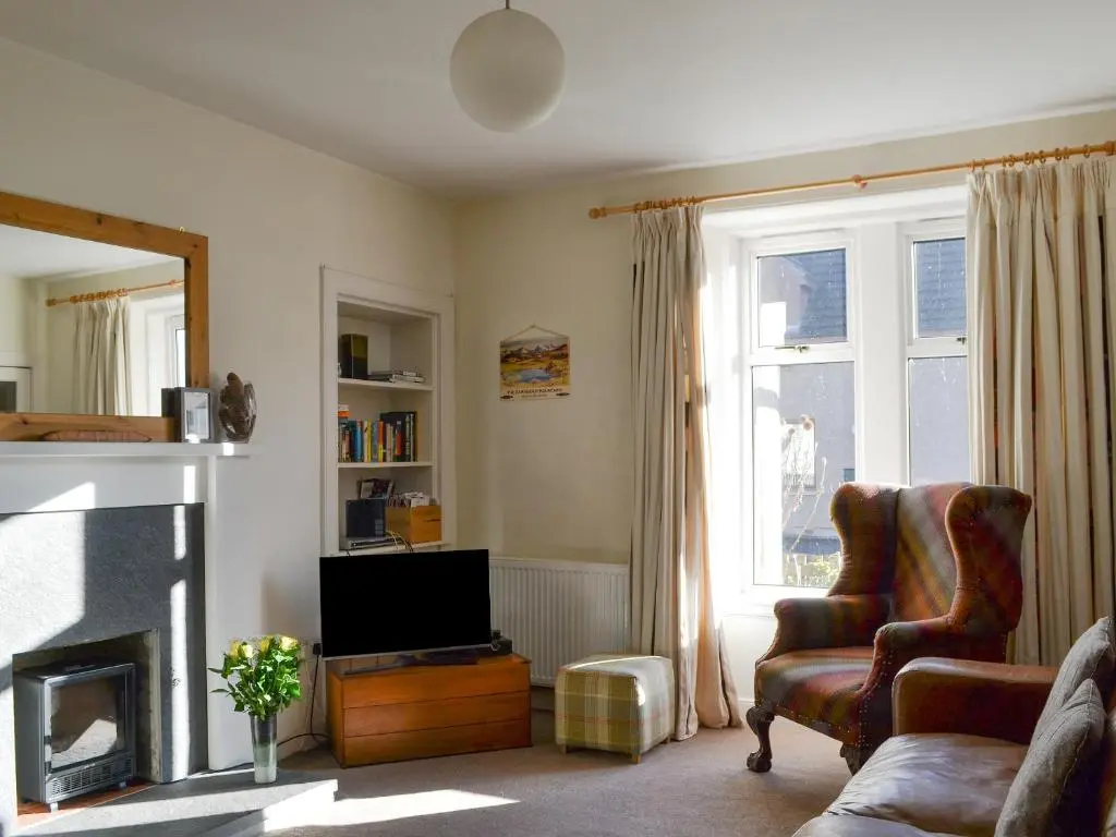 a living room with a fireplace and a chair and a television at Langside in Kingussie