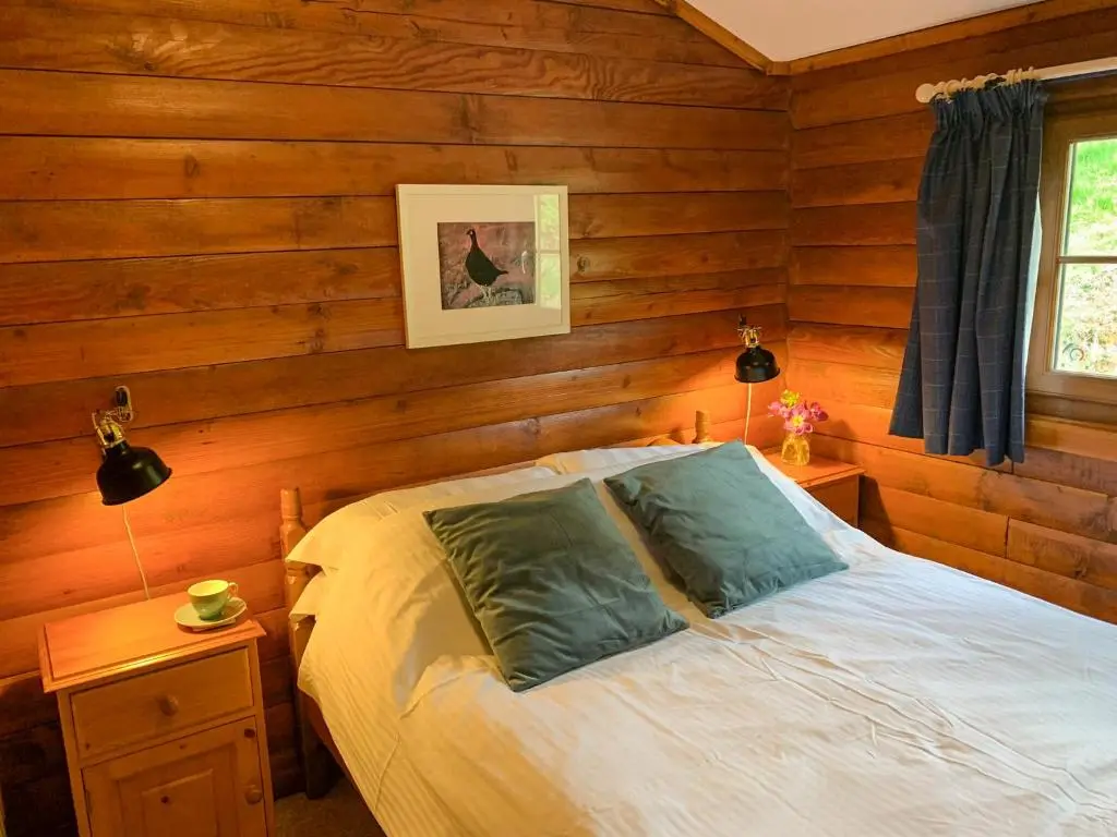 a bedroom with a bed with wooden walls and a window at Squirrel View in Newtonmore