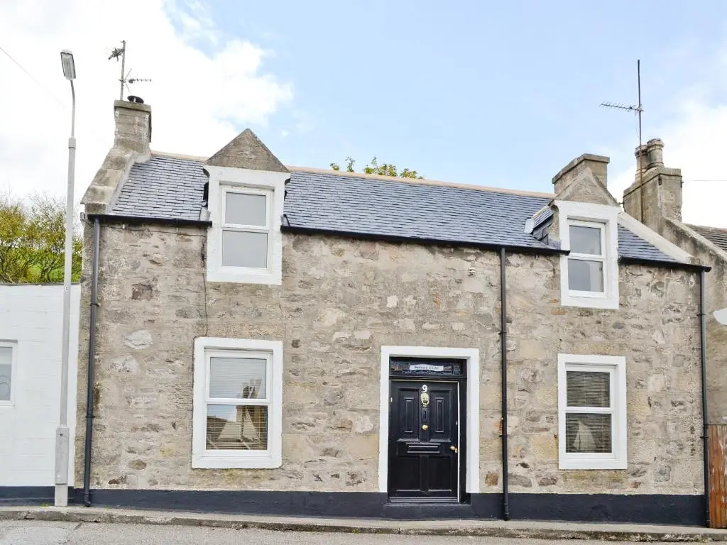 a stone house with a black door and white windows at Boatmans Cottage - 27787 in Portessie