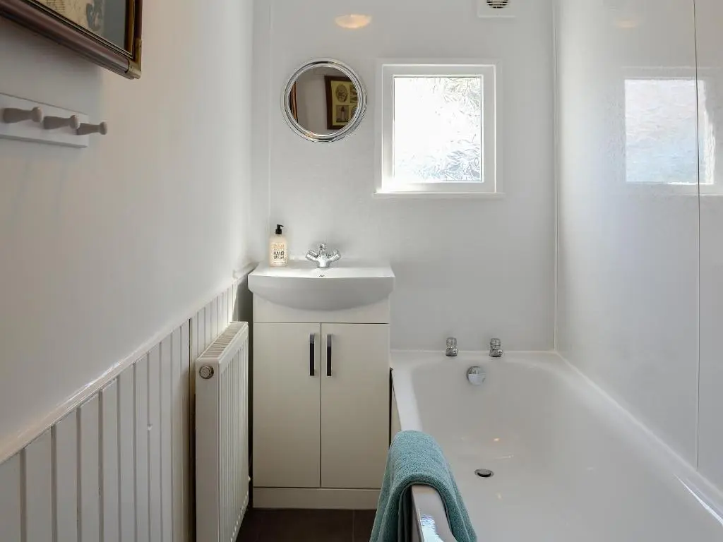 a white bathroom with a sink and a bath tub at Boatmans Cottage - 27787 in Portessie