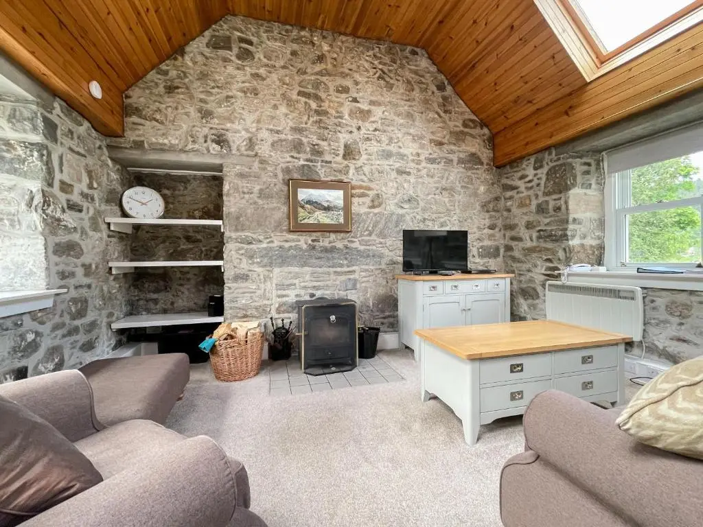 a living room with a stone wall at Glacour Studio Cottage in Bridgend