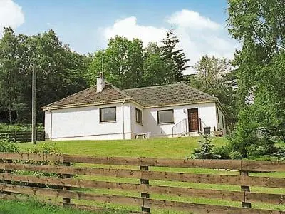 a white house in a field with a fence at Holly Cottage in Gorstan
