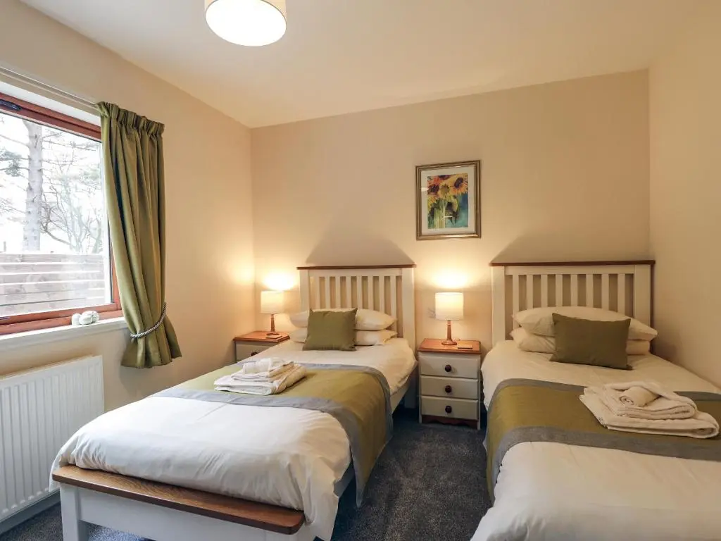 two beds in a room with two lamps and a window at Holly Cottage in Gorstan