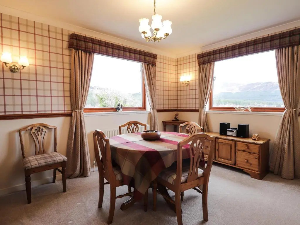 a dining room with a table and chairs and two windows at Holly Cottage in Gorstan