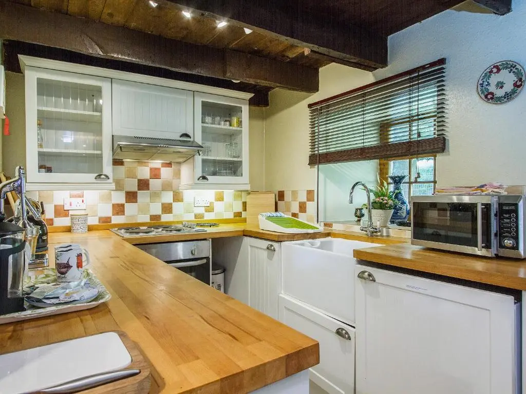 a kitchen with white cabinets and a wooden counter top at Gardener's Bothy in Balnaboth