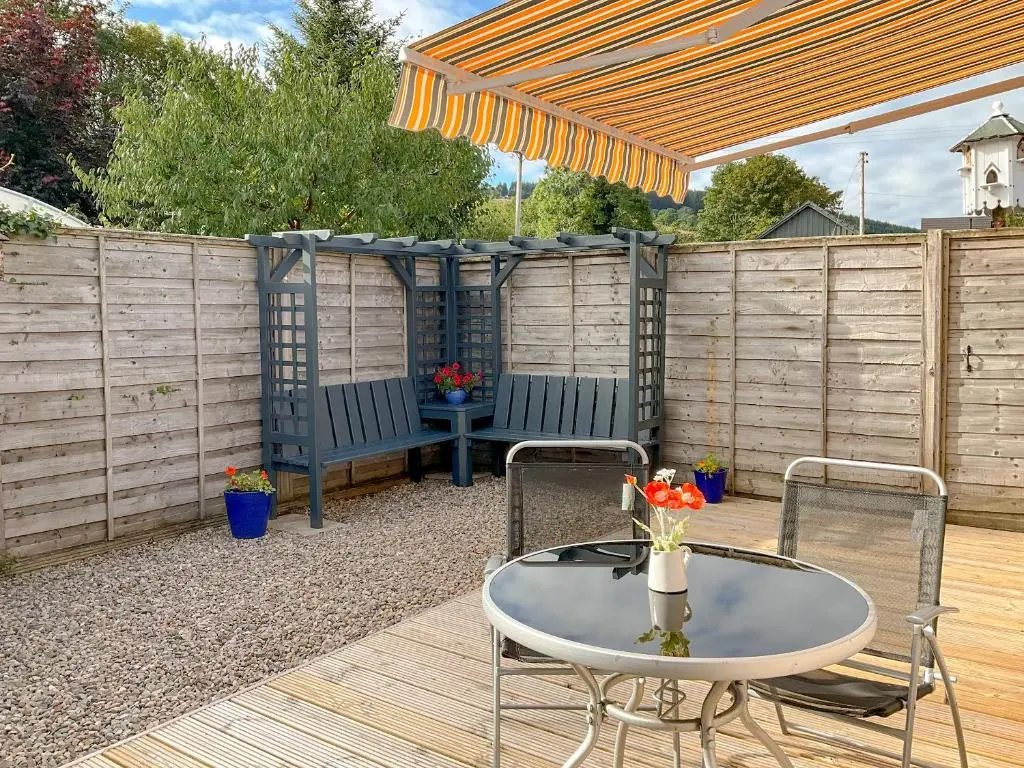 a patio with a table and chairs and a fence at Thistle Dubh in Drumnadrochit