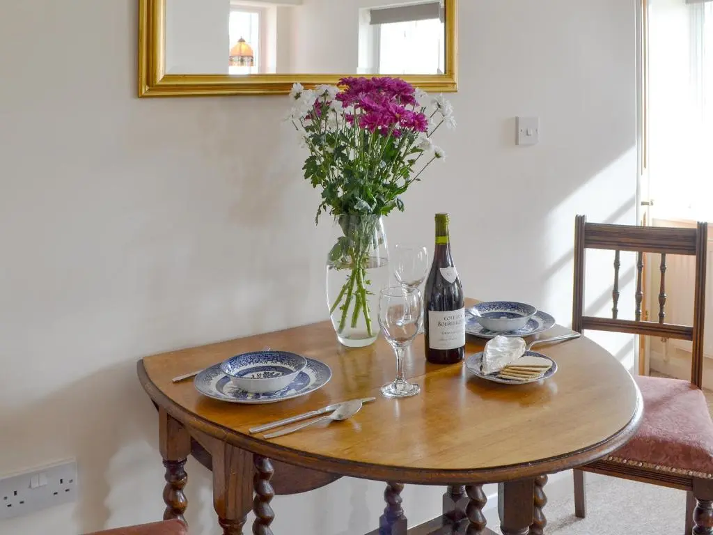 a table with a vase of flowers and a bottle of wine at Temple House West in Drumnadrochit