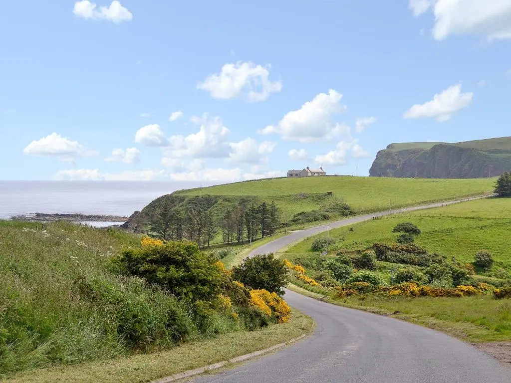 a winding road on a hill with a house in the distance at Pennan Lodge - 26818 in Pennan