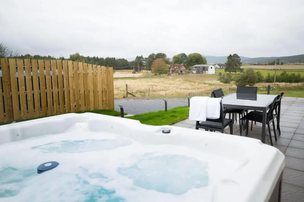 a hot tub on a patio with a table and chairs at Tomdhu Lodge - Seasgair Lodges in Boat of Garten