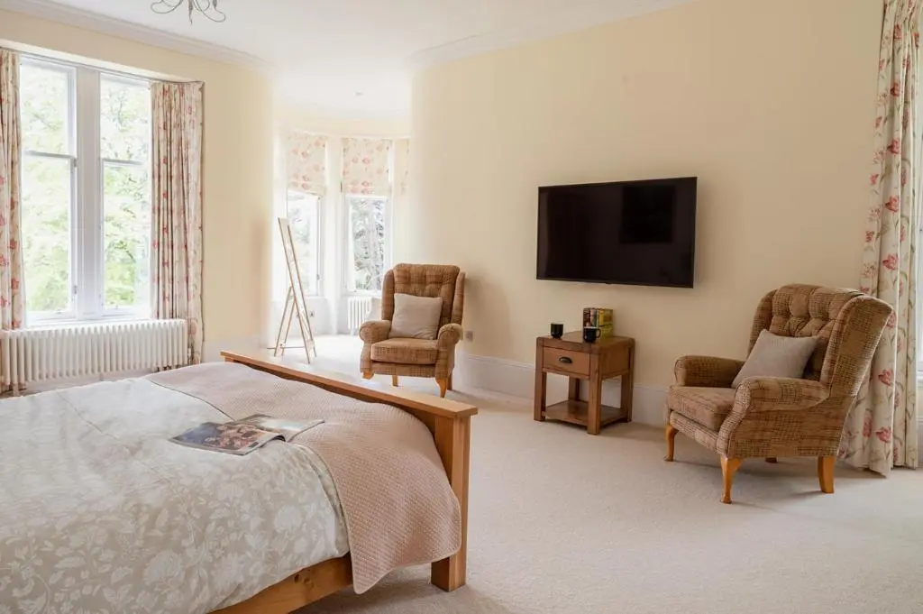 a bedroom with a bed and two chairs and a television at Craigard Lodge - Seasgair Lodges in Boat of Garten