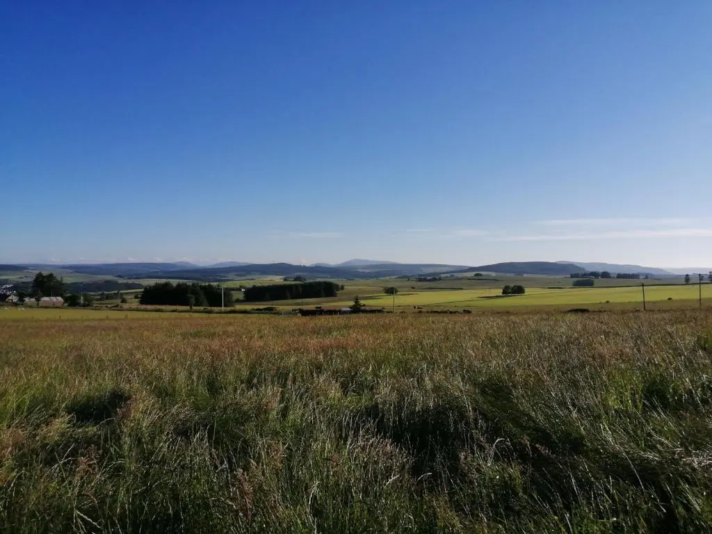 a field of grass with hills in the background at Knockan in Keith
