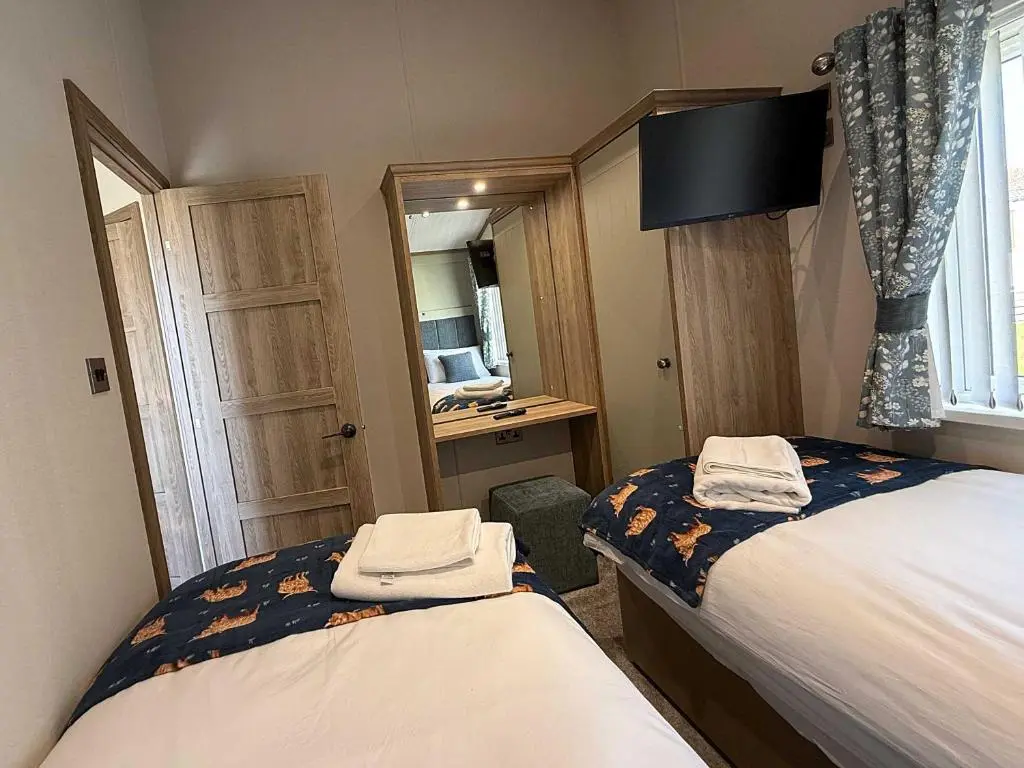 a small bedroom with two beds and a mirror at Highland Holiday Getaways - The Heilan' Lodge in Embo