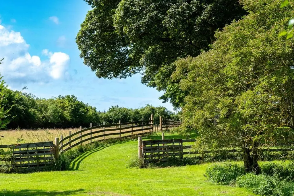 a wooden fence in a field with a tree at Marcassie Farm Lodges - Willow Studio in Forres