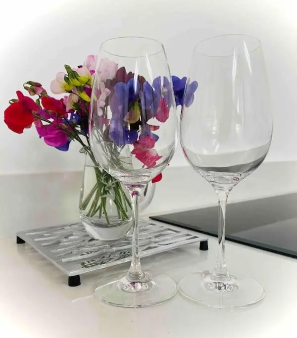 two wine glasses and a vase of flowers on a shelf at Lily Cottage - 1 bedroom in Forres