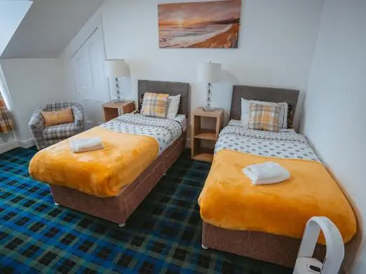 a bedroom with two beds and a chair at Nairn View Guest House in Nairn