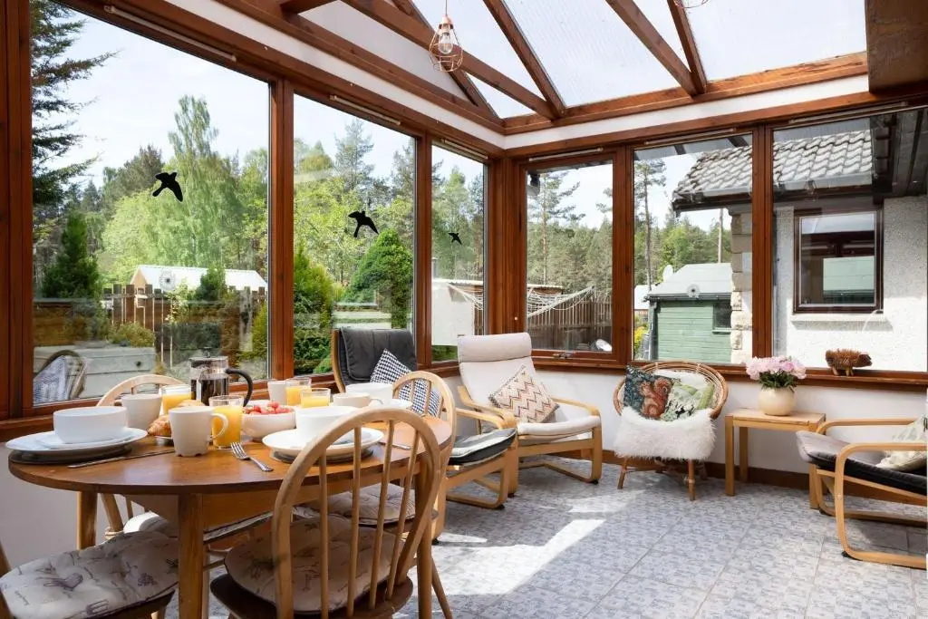 a conservatory with a table and chairs and windows at Langrick in Nethy Bridge
