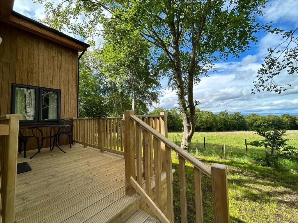 a wooden deck next to a house with a tree at Breckland Lodge 3 with Hot Tub in Belladrum