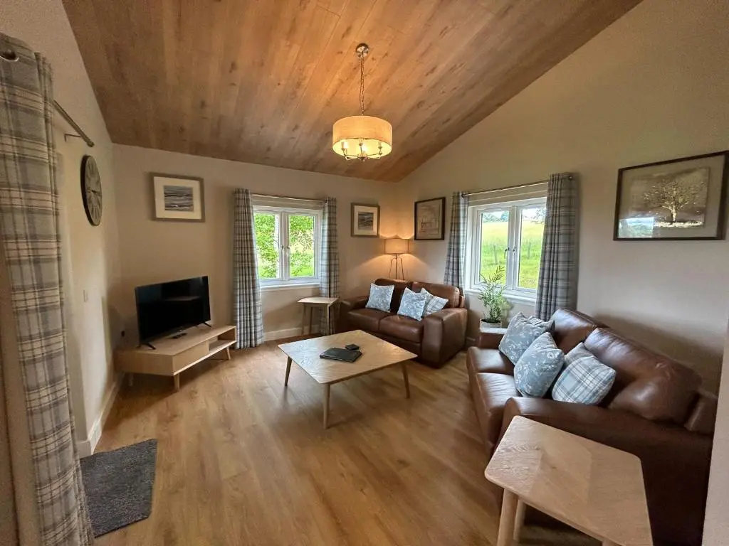 a living room with a couch and a tv at Breckland Lodge 3 with Hot Tub in Belladrum