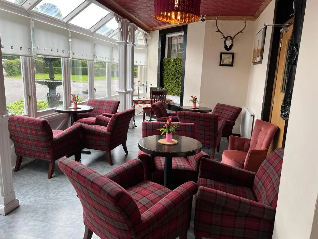 a restaurant with red chairs and tables and windows at Strathpeffer Hotel in Strathpeffer