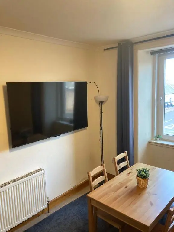 a living room with a table and a large tv on the wall at 2 Bed Central Ness Apart - May Court in Inverness
