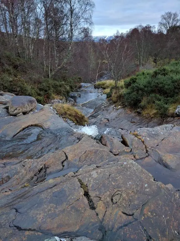 a river with rocks and water in a field at Cluny Mains in Newtonmore