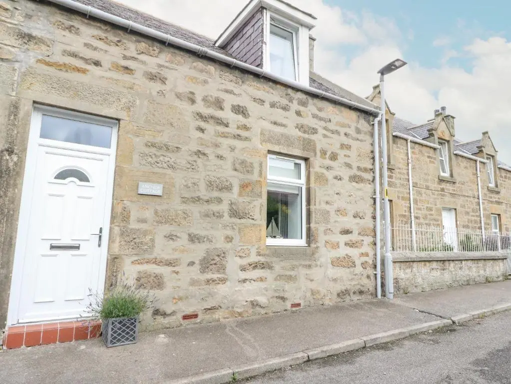 a stone house with a white door and a street at Anchor Cottage in Elgin