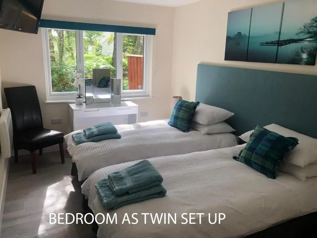 a bedroom with two beds and a chair and window at The South Cabin at Easter Arr in Nairn