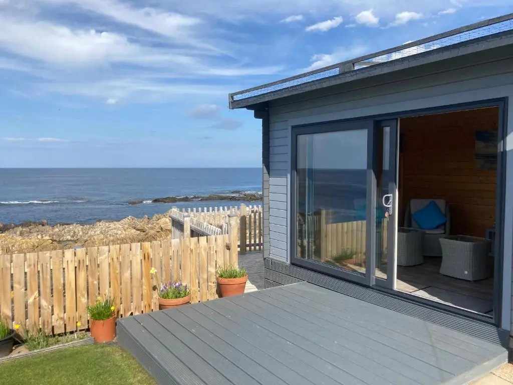 a house with a deck with the ocean in the background at Seafront holiday home in Findochty in Findochty