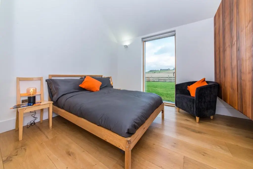 a bedroom with a bed and a chair and a window at The Den, Architect Designed Barn, Beautiful Location in Kirkton of Skene
