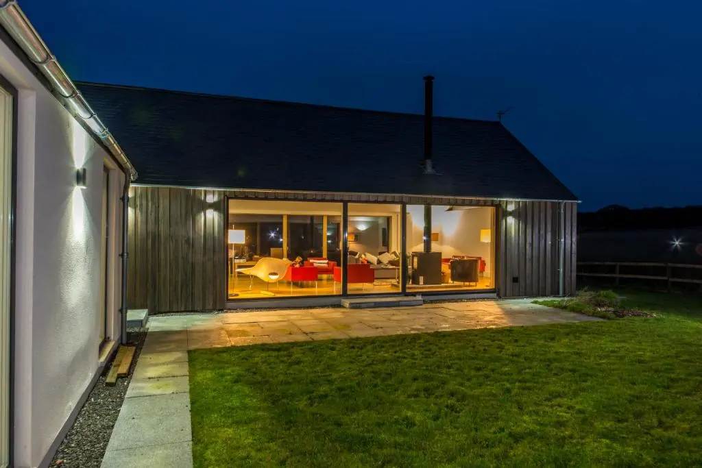 a house with a view of the backyard at night at The Den, Architect Designed Barn, Beautiful Location in Kirkton of Skene